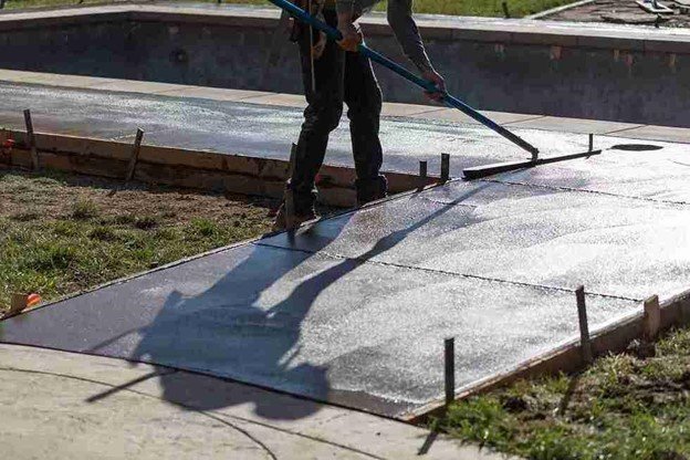 Concrete driveway installation with a worker smoothing freshly poured surface using a finishing tool in Shaker Heights, OH