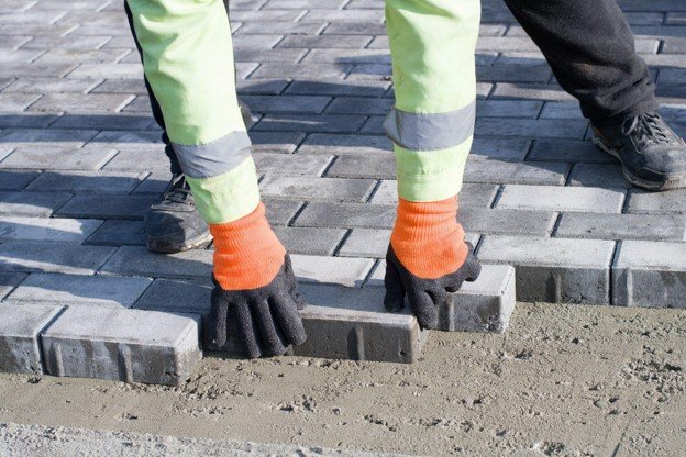 Concrete contractor placing brick pavers by hand for residential driveway installation in Parma Heights, OH