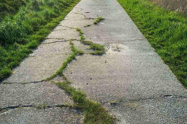 Cracked and damaged concrete driveway with visible wear and weeds growing through the surface in Shaker Heights, OH